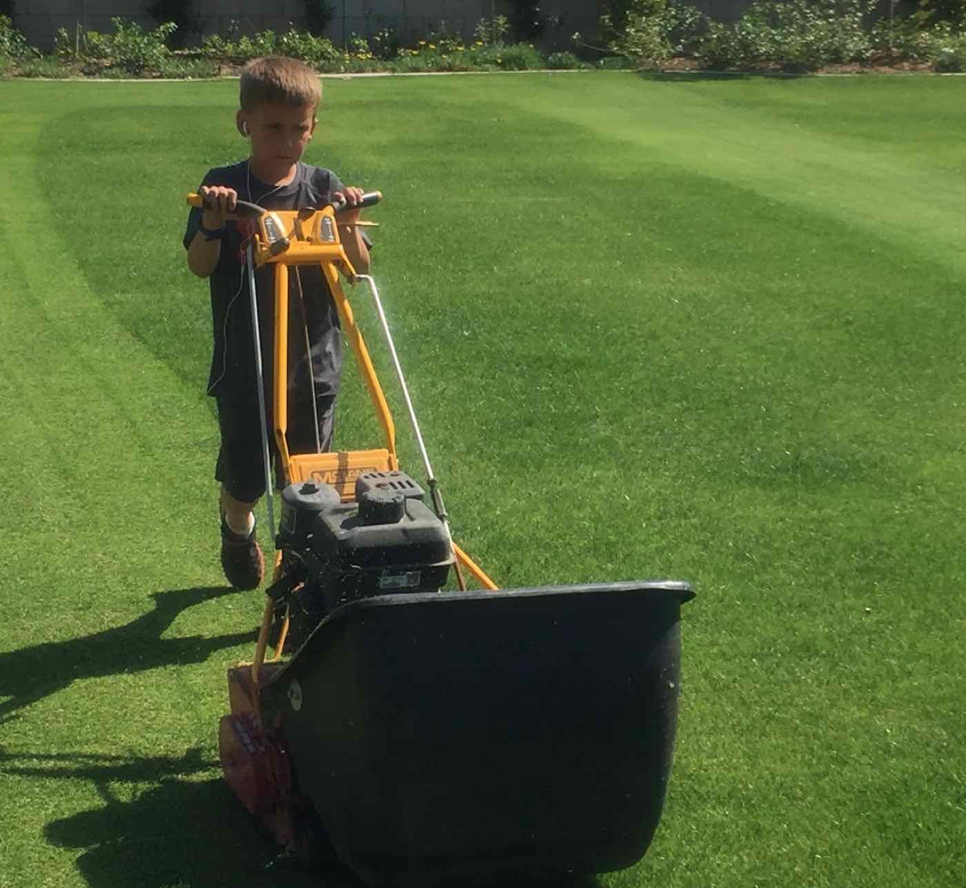 Young Blake pushing a mower across a striped lawn