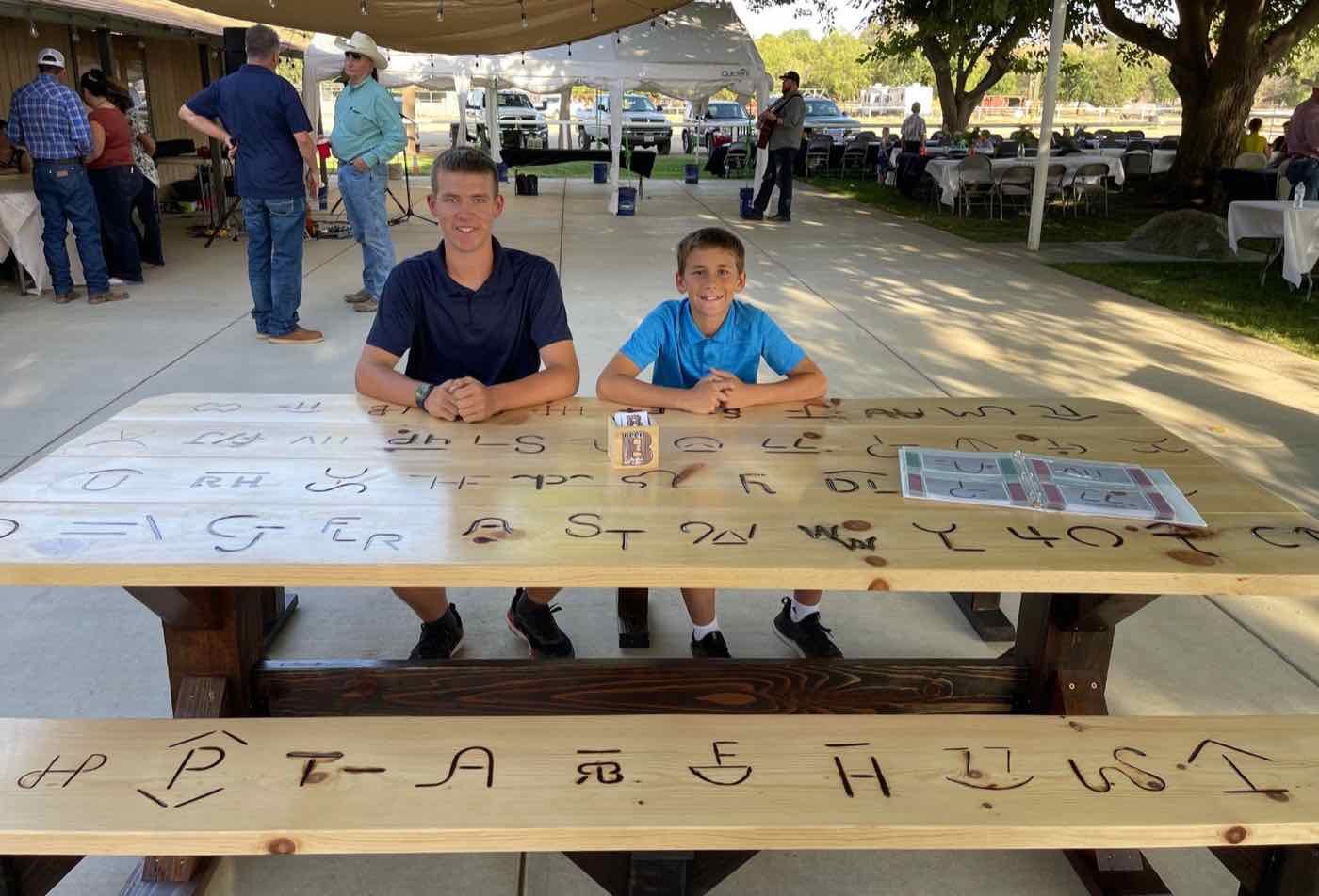 Zachary and Blake seated at a large picnic table with cattle brands burned into the top
