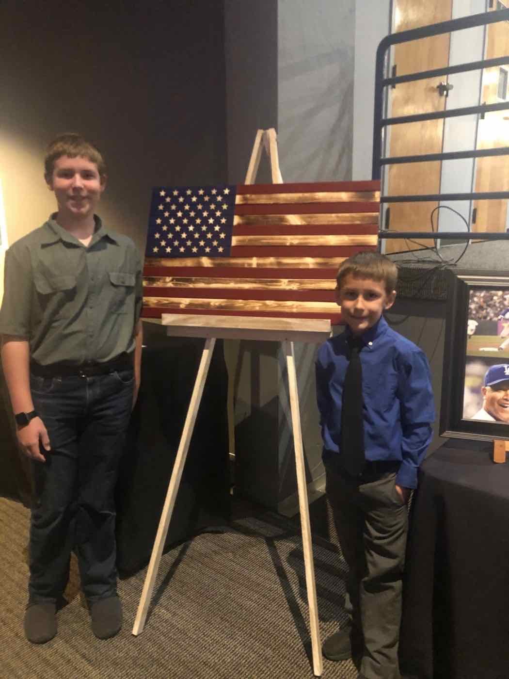 Zachary and Blake beside a handmade wooden flag donated to a charity event