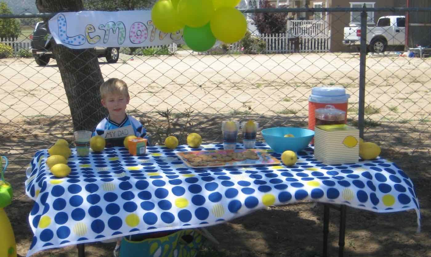 Young Zachary at his lemonade stand with a blue polka dot tablecloth and balloons