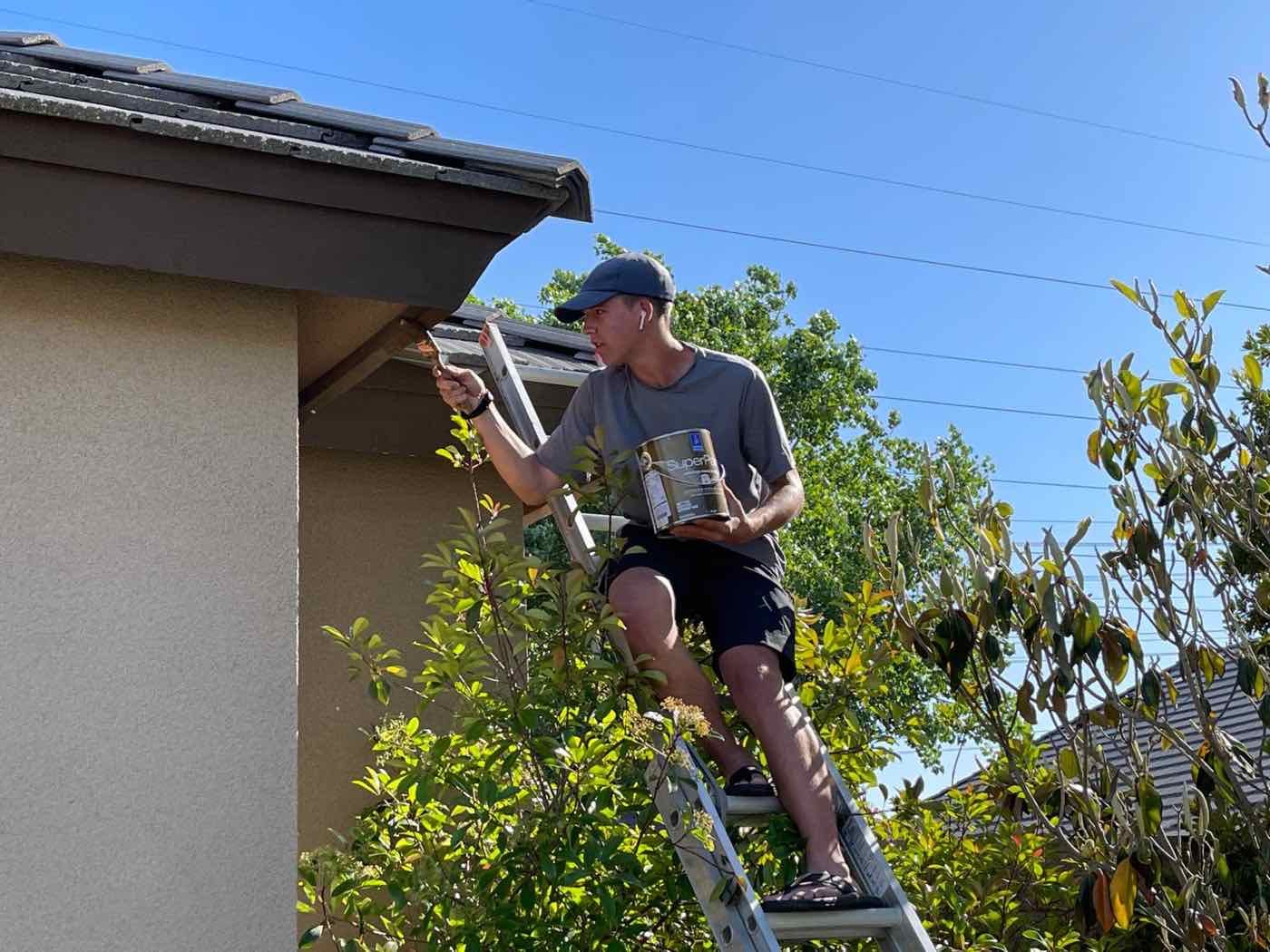 Zachary on a ladder painting the eaves of a house