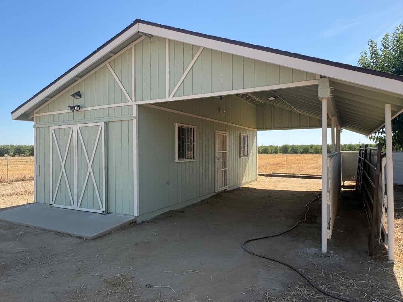 The same barn repainted sage green with crisp white trim and posts