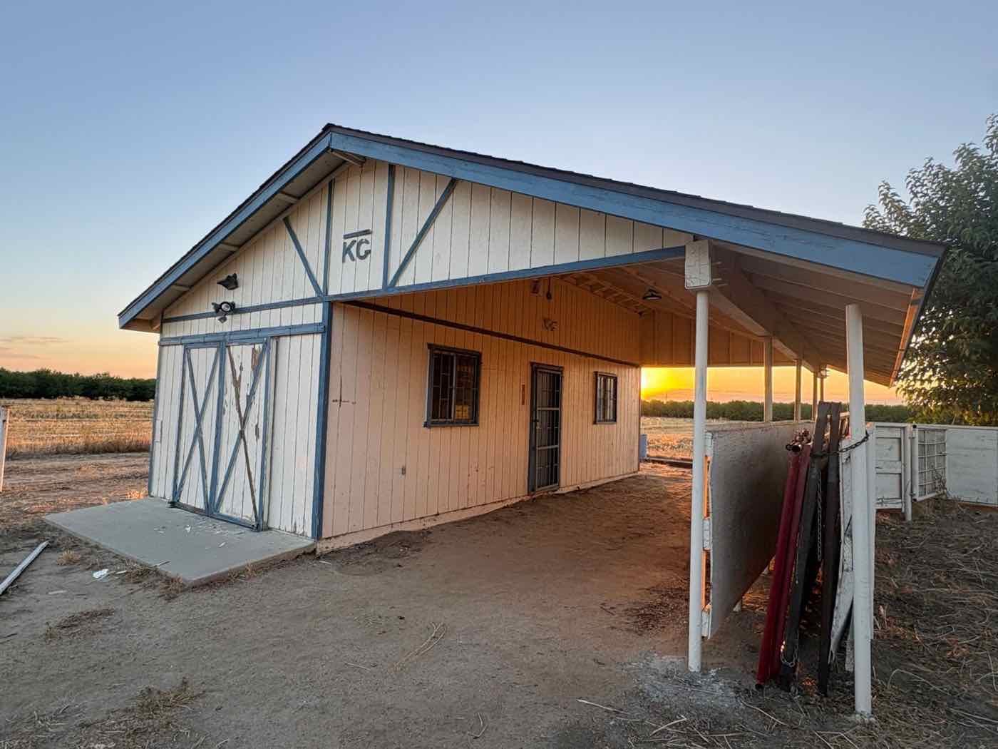 Barn with a covered side stall, faded white paint and peeling blue trim, before repainting