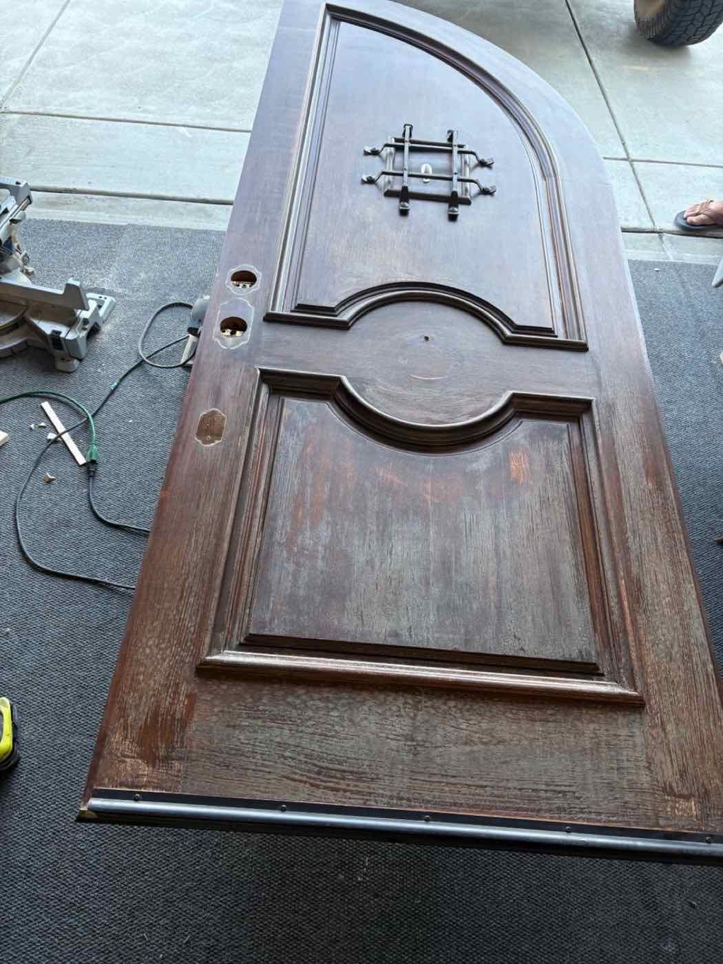 Arched wood front door laid flat and partly sanded, before refinishing
