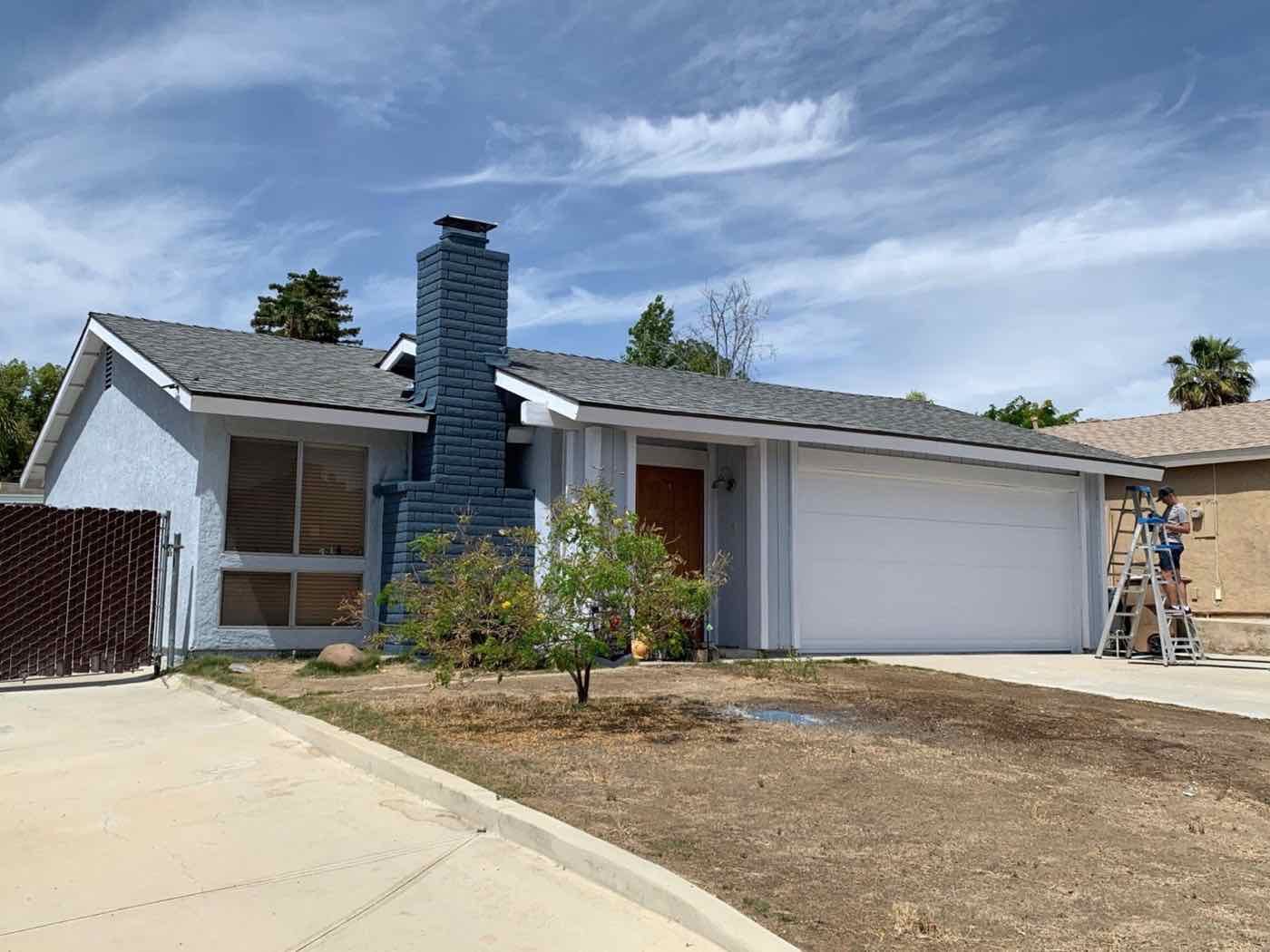 Single-story home freshly painted blue-gray with a navy brick chimney and white garage door