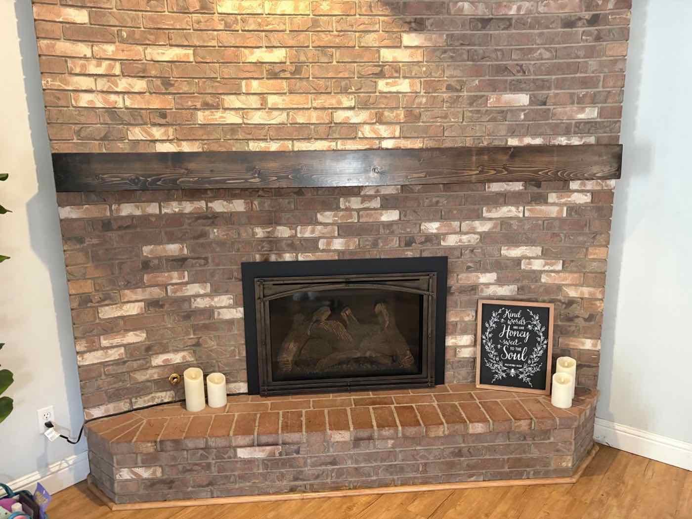 Custom dark stained wood beam mantel on a brick fireplace wall