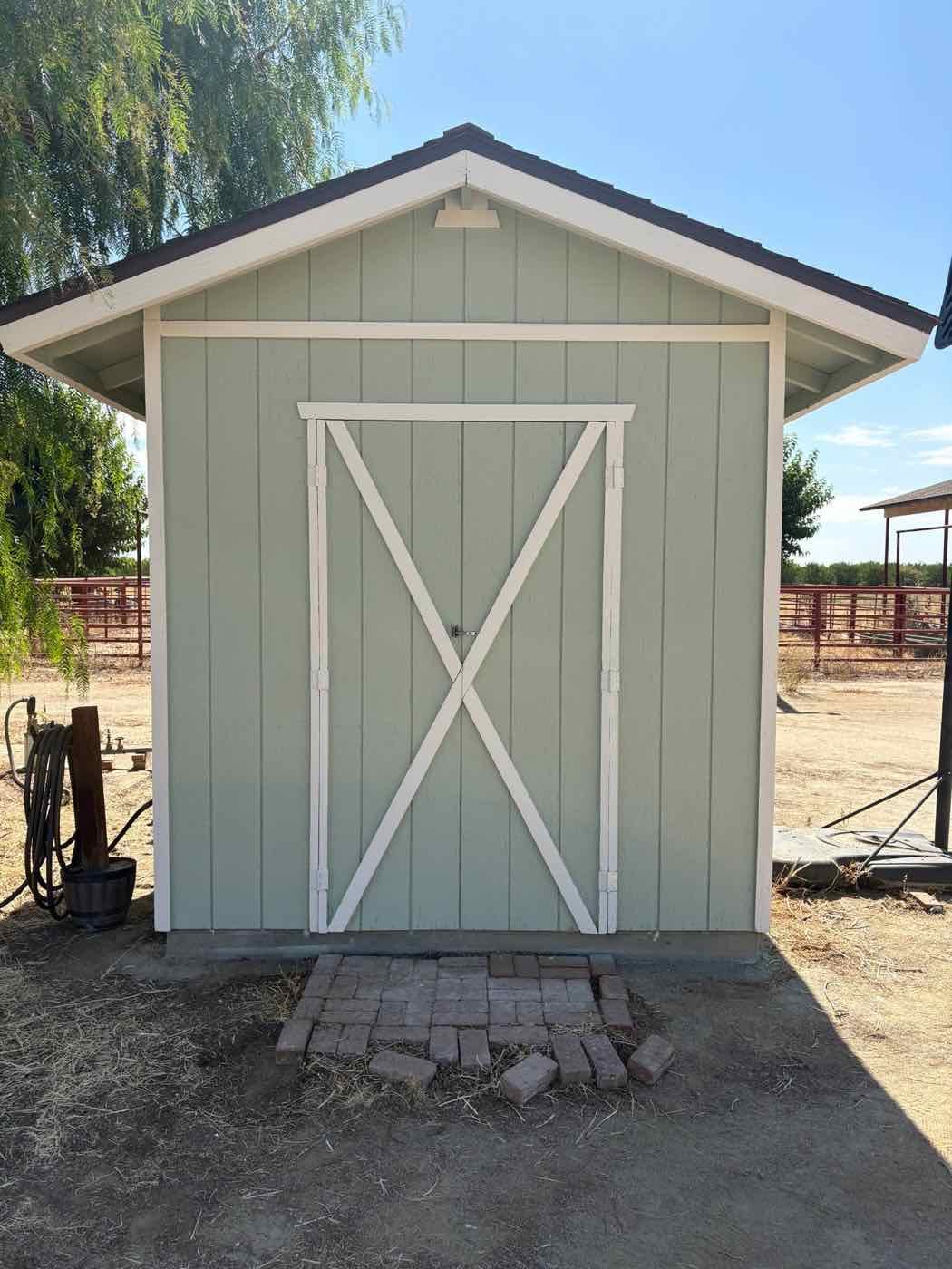 The same shed repainted sage green with white X-brace doors and trim