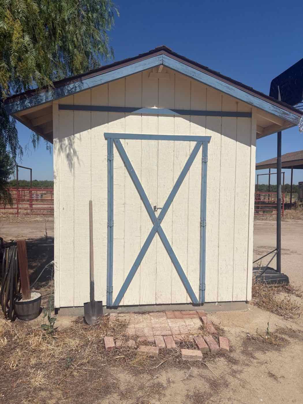 Small storage shed in cream with faded blue trim, before repainting
